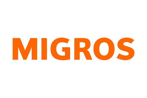 Das Bild zeigt das Wort MIGROS in fetten, orangefarbenen Großbuchstaben auf einem hellgrauen Hintergrund.